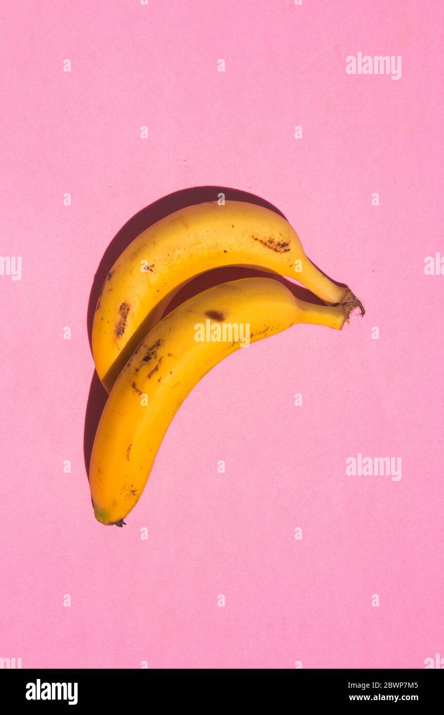 Colpo chiuso di due banane gialle con macchie scure su una superficie rosa con forte luce solare Foto Stock