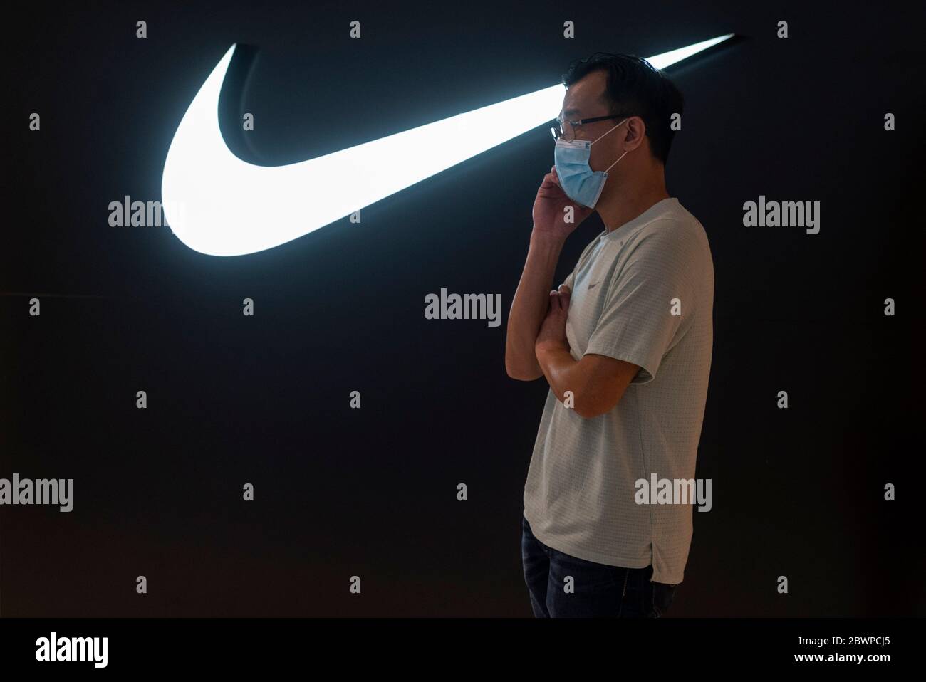 Un uomo che indossa una maschera parla al telefono mentre indossa una  maschera di fronte al marchio internazionale di abbigliamento sportivo  americano negozio Nike e logo visto in un centro commerciale di