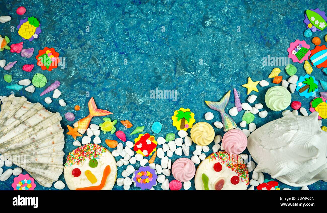 Tema estivo della spiaggia flatlay con conchiglie reali e caramelle, ciottoli, code di pesce, icone di festa estiva e biscotti volti su uno sfondo blu textured con neg Foto Stock