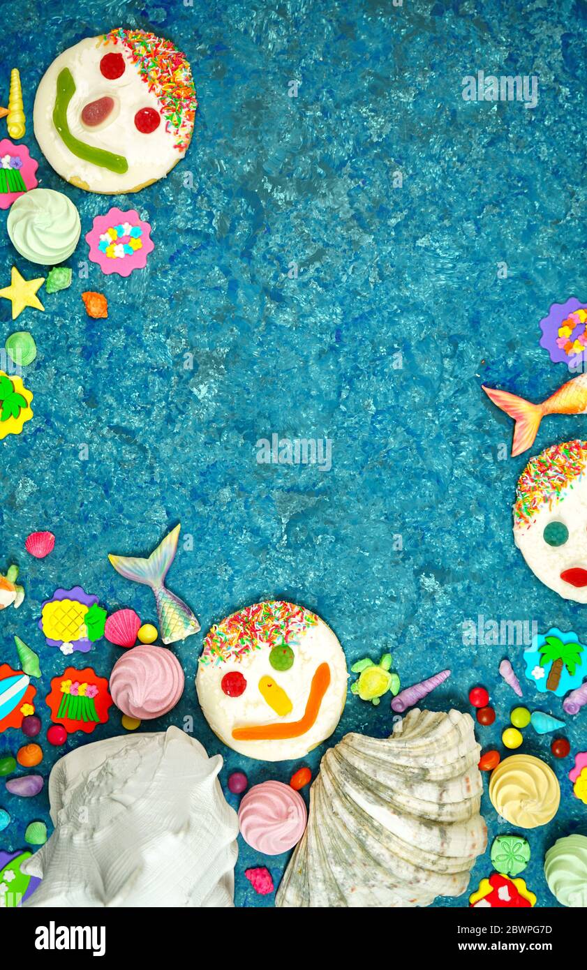 Tema estivo della spiaggia flatlay con conchiglie reali e caramelle, ciottoli, code di pesce, icone di festa estiva e biscotti volti su uno sfondo blu textured con neg Foto Stock