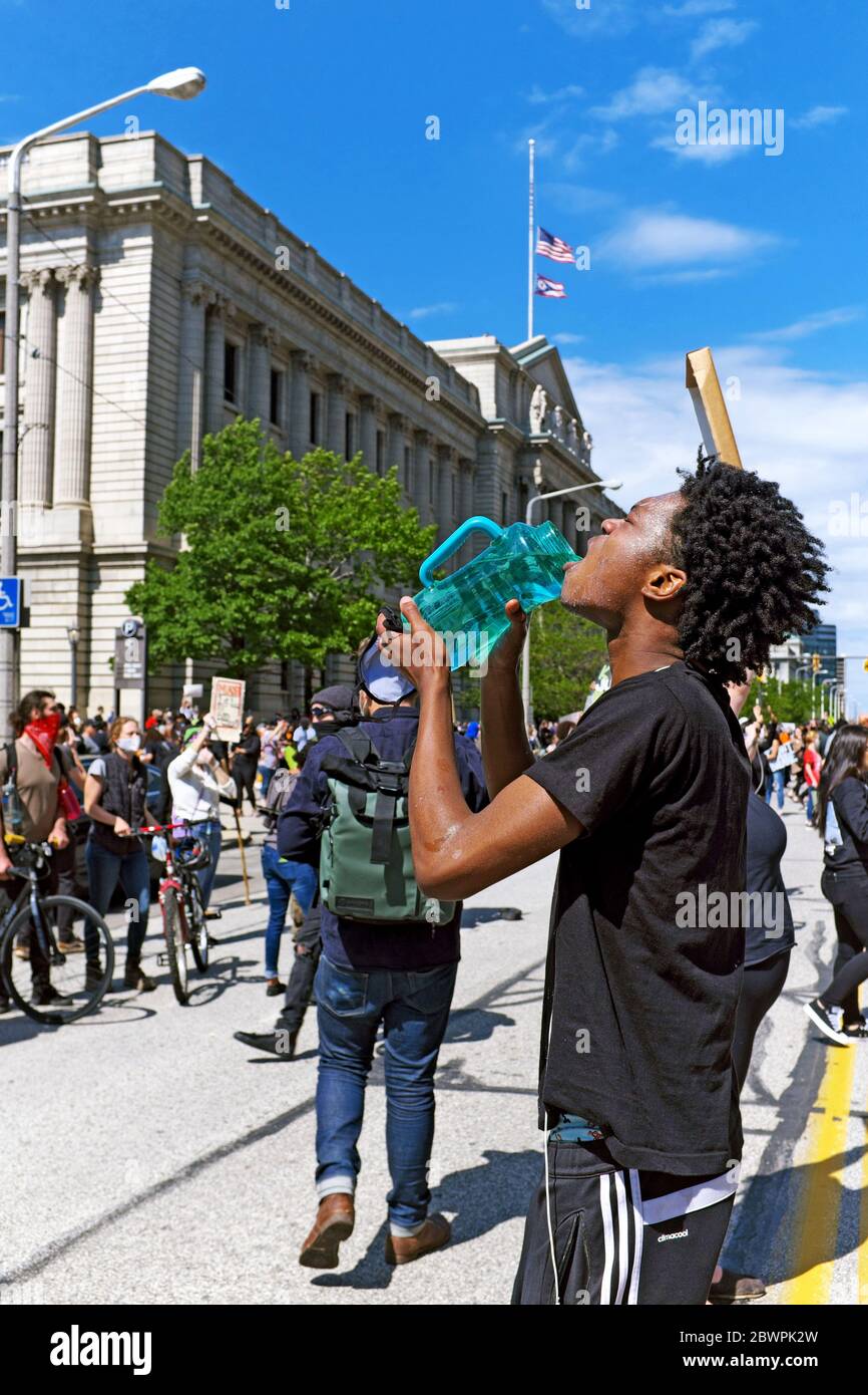 Un giovane uomo nero si tratta per gas lacrimogeni da Cleveland Police durante il 30 maggio 2020, Black Lives materia di protesta che si è trasformato in ciò che è stato chiamato una rivolta. L'uomo nero ha le sue spalle all'epicentro della protesta si è rivolta, il Cleveland Justice Center edificio su Lakeside Avenue nel centro di Cleveland, Ohio, Stati Uniti. Foto Stock
