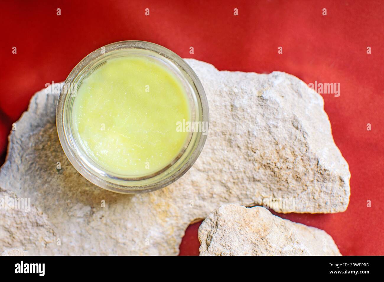 Crema cosmetica in un vaso su fondo marrone o rosso e pietre naturali. Ingredienti naturali e materiali ecocompatibili. Foto Stock