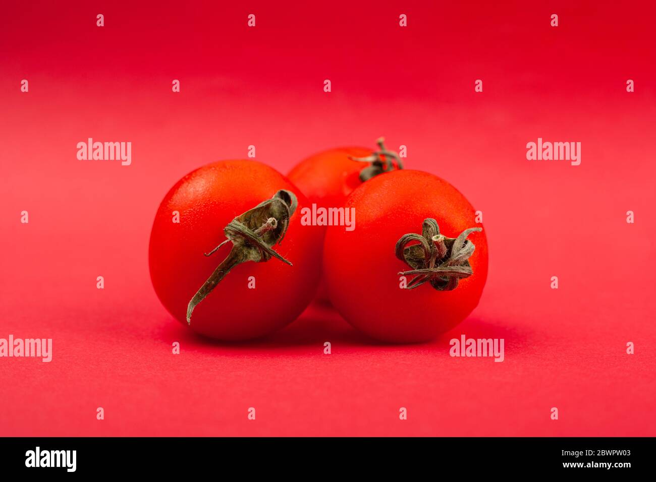 tre pomodori succosi rotondi su sfondo rosso da vicino. Foto Stock