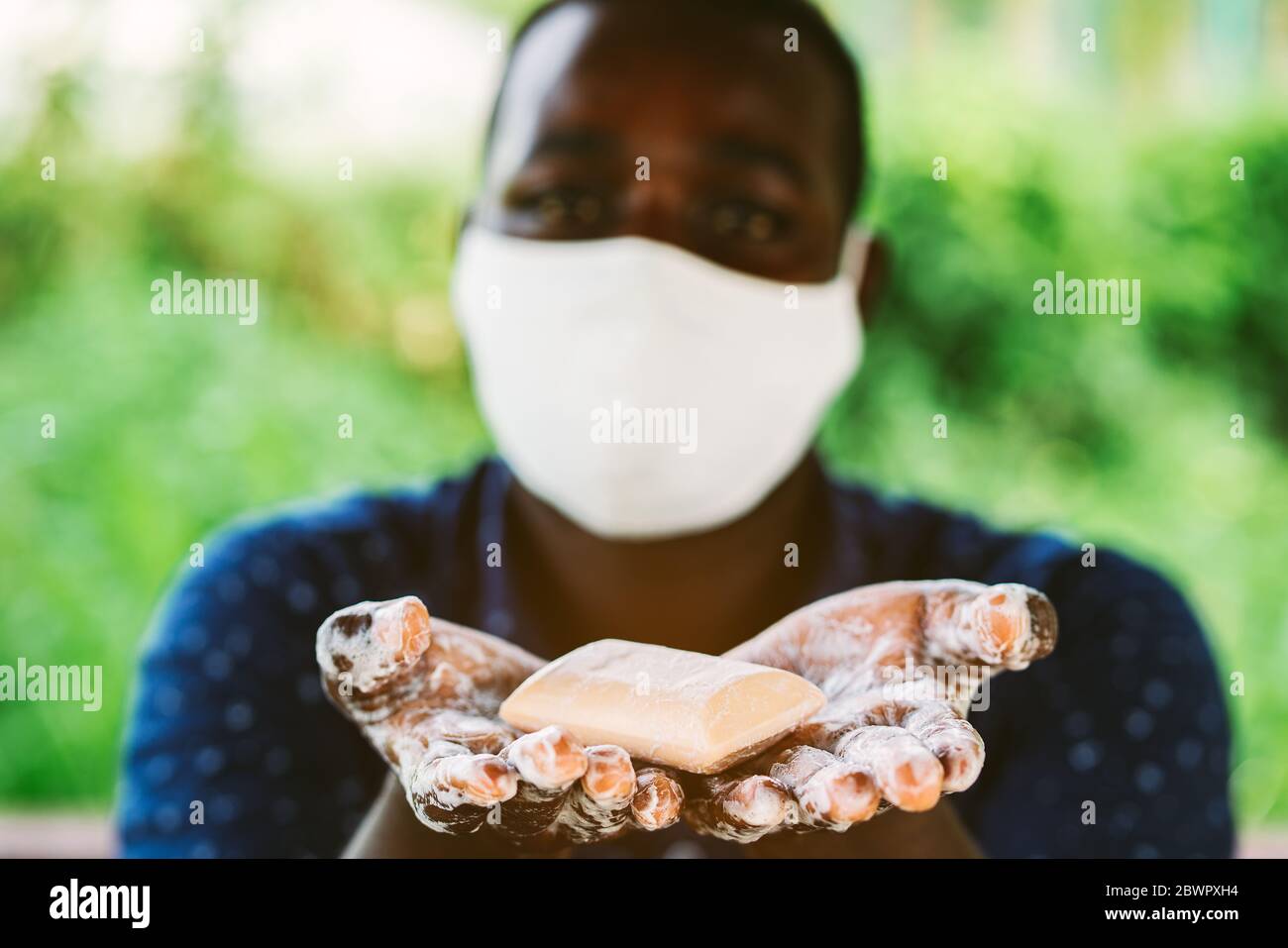 L'uomo africano tiene e mostra un pezzo di sapone bagnato con maschera di indossare Foto Stock