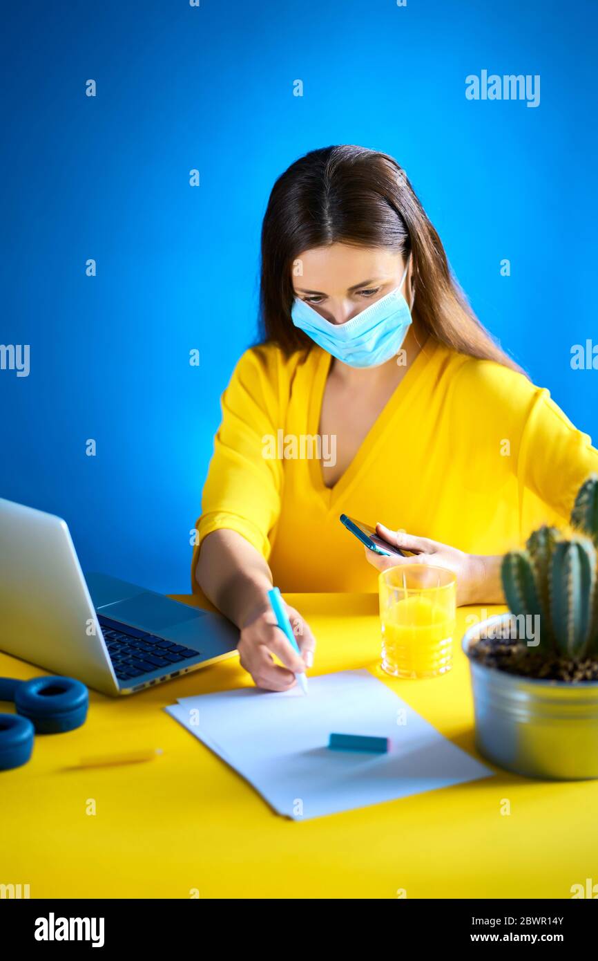 donna in una blusa gialla lavora a distanza a casa durante una pandemia Foto Stock