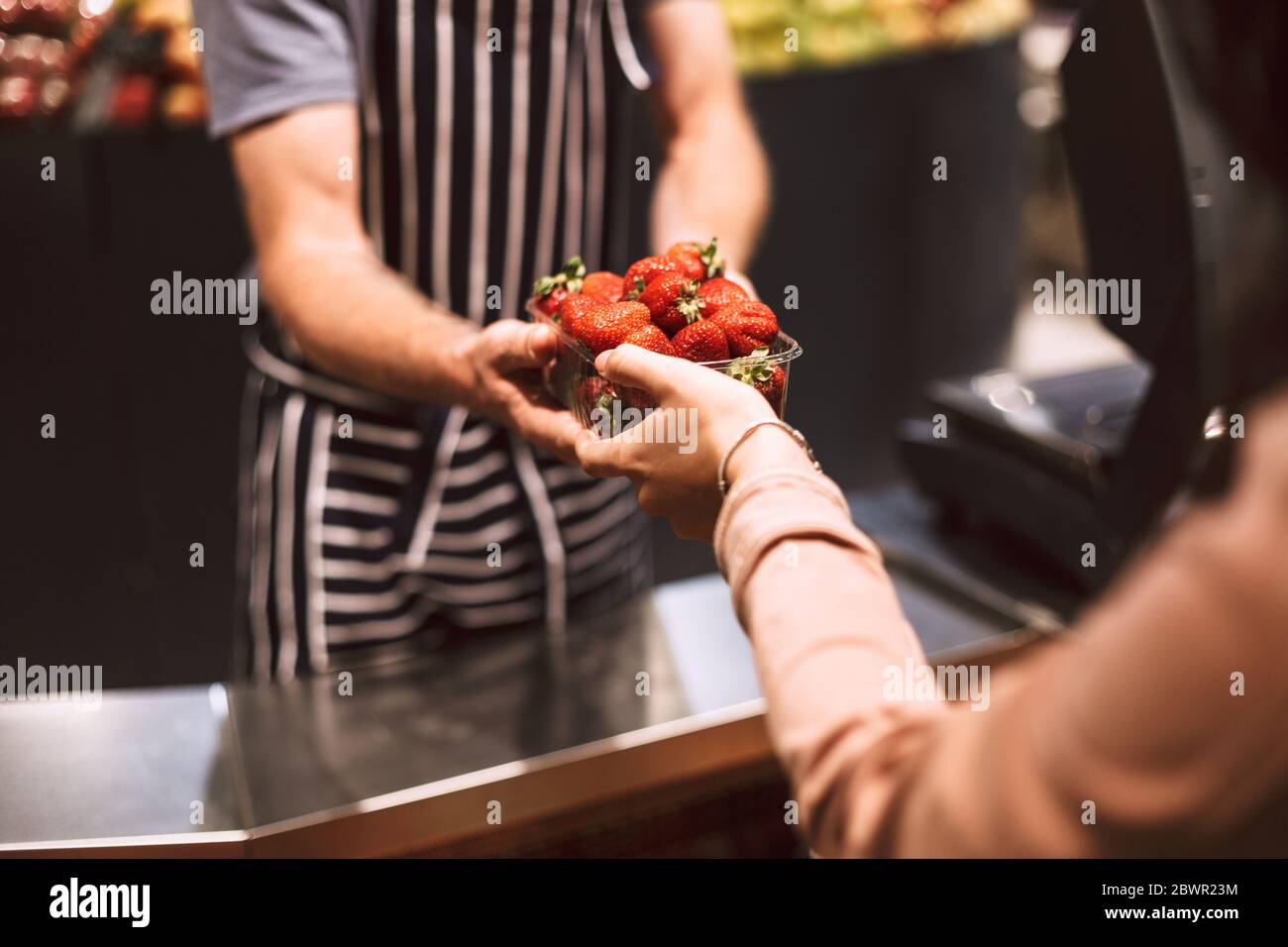 Primo piano venditore in grembiule a strisce dietro il bancone dando fragole al cliente in un moderno supermercato isolato Foto Stock