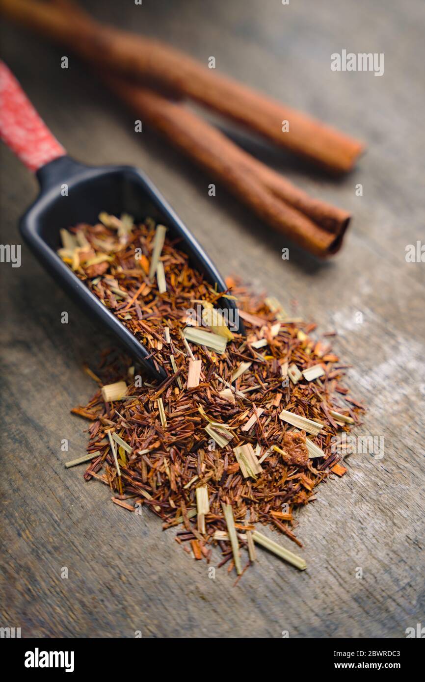 Primo piano di una manciata di foglie di rooibos poste su una superficie di legno con un cucchiaio da tè giapponese Foto Stock