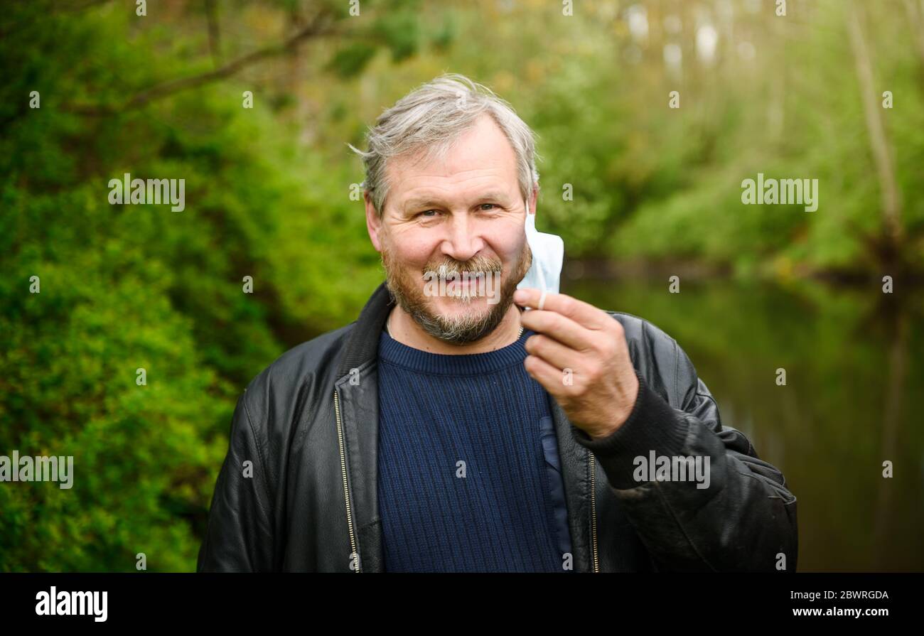 Un uomo felice di mezza età rimuove una maschera medica dal viso in un parco primaverile. Sopra il coronavirus. Fine della pandemia, epidemia e quarantena. Foto Stock