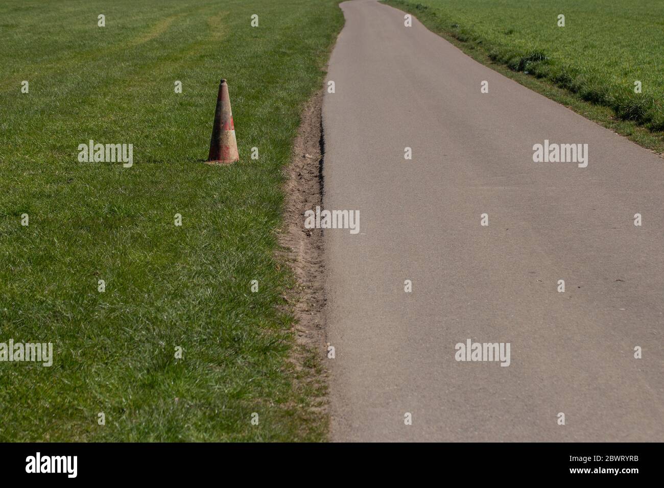 Cono di traffico sporco e intemperie nell'erba accanto a una strada con spazio per la copia Foto Stock