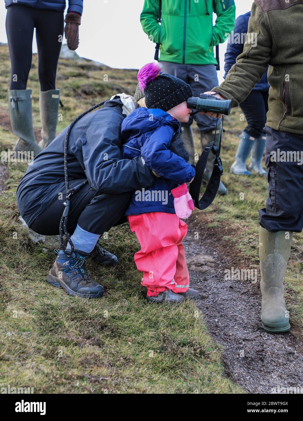 Un bambino di 3 anni che guarda attraverso il binocolo tenuto dai nonni in una passeggiata in inverno, Inghilterra, Regno Unito Foto Stock
