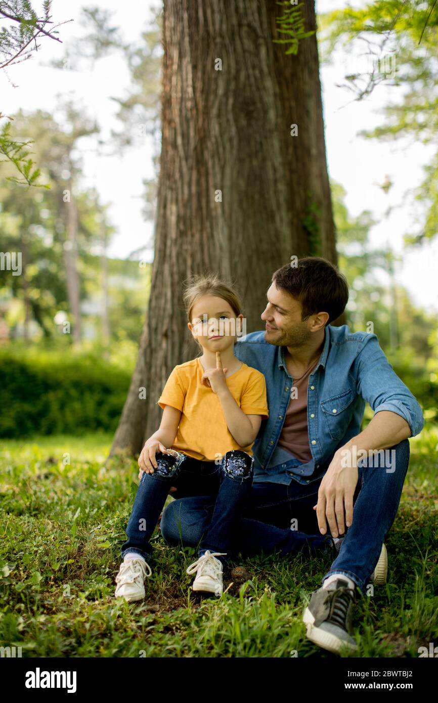 Un solo padre seduto sull'erba dall'albero con la piccola figlia carina Foto Stock