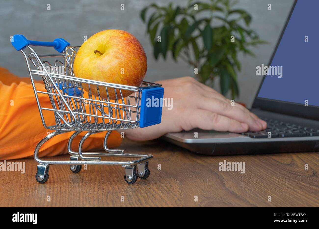 carrello con mela. fuoco selettivo. in background, un uomo ordina un prodotto su un portatile. shopping online Foto Stock