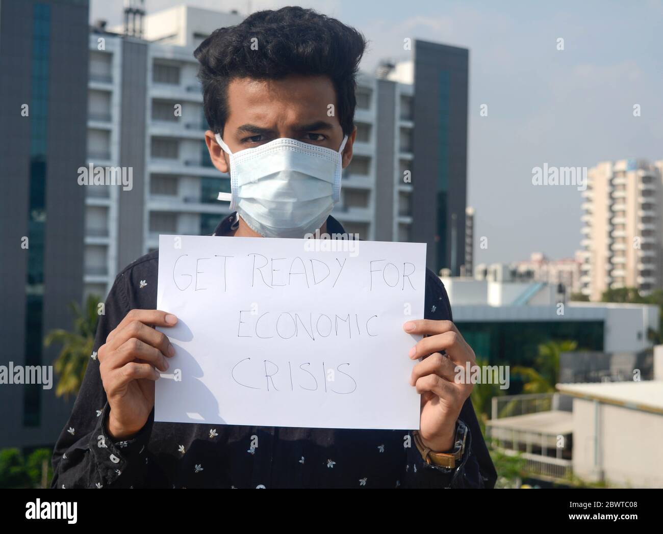 Uomo che indossa maschera medica e tenere in mano carta bianca con un testo di prepararsi per la crisi economica. Foto Stock