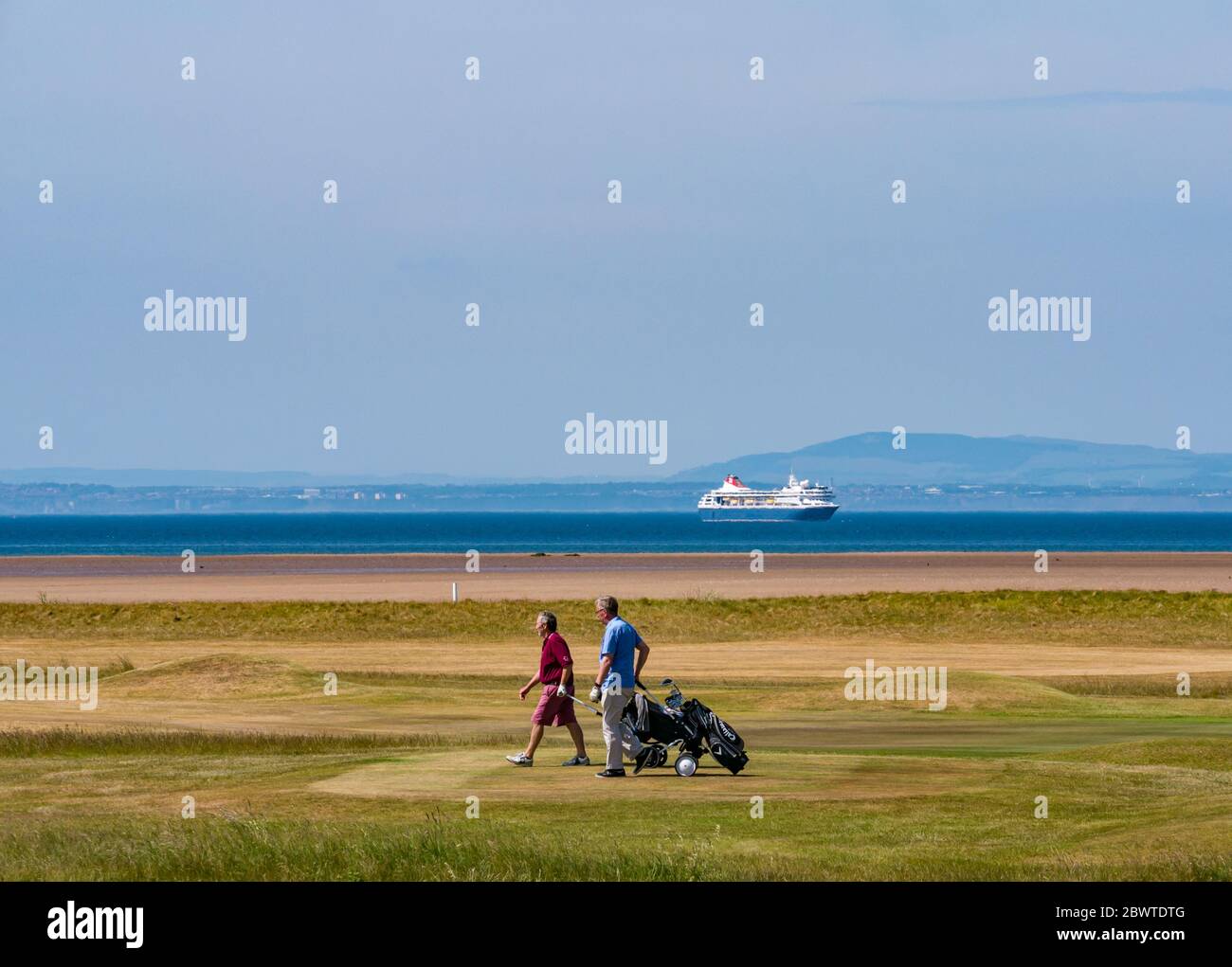 Golfisti con golf cart sul campo da golf Kilspindie con la nave da crociera Fred Olsen ancorata a Firth of Forth, East Lothian, Scozia, Regno Unito Foto Stock