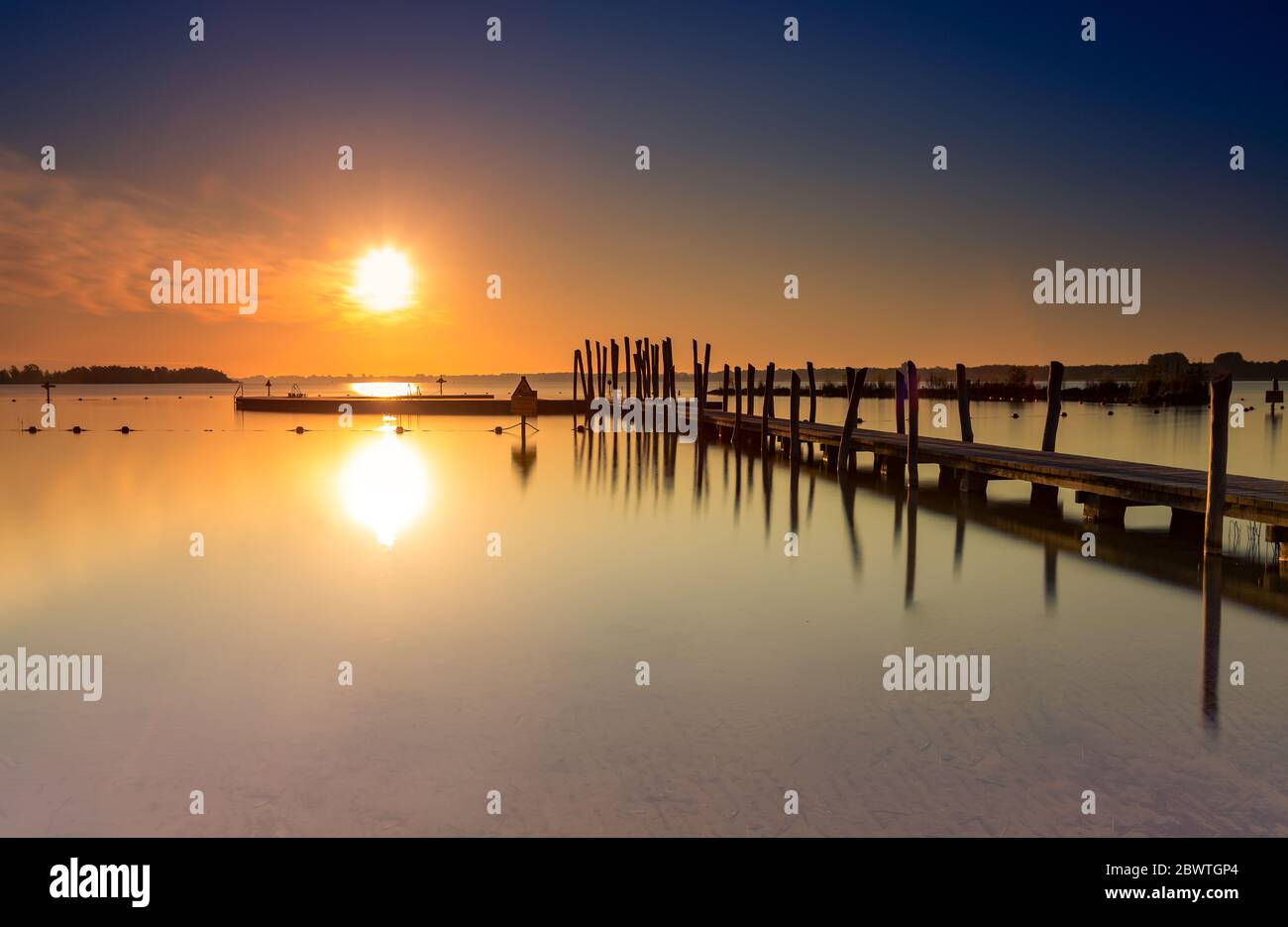 Molo sulla spiaggia e piscina all'aperto presso il lago Wijderwold durante un'impressionante alba a Zeewolde, Paesi Bassi. (esposizione lunga) Foto Stock