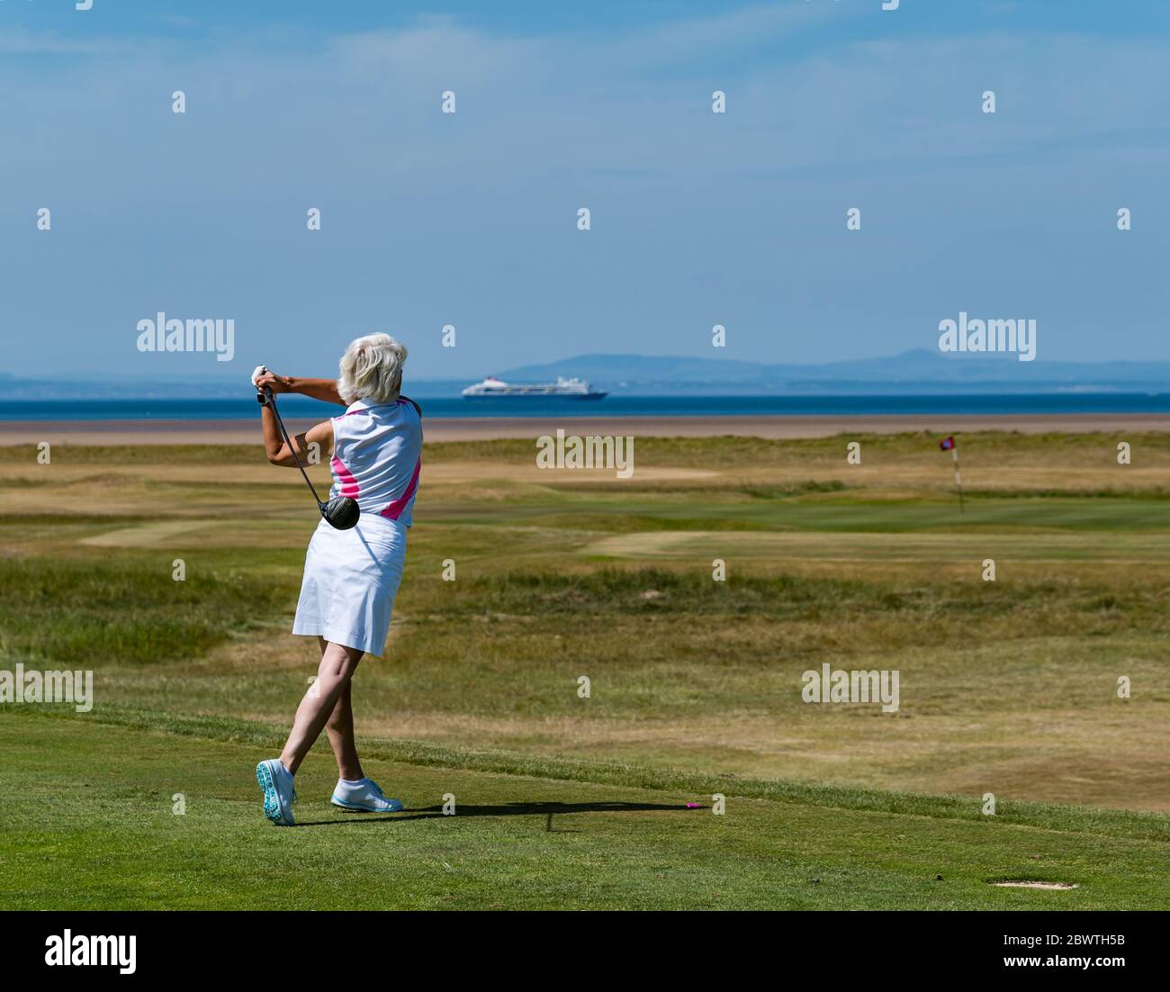 Golfista femminile che colpisce la sfera di golf sul campo da golf con vista di Firth of Forth, East Lothian, Scozia, Regno Unito Foto Stock