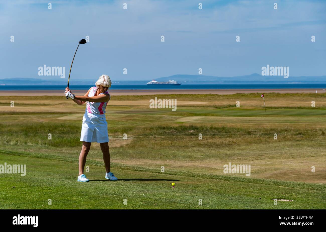 Golfista femminile che colpisce la sfera di golf sul campo da golf con vista di Firth of Forth, East Lothian, Scozia, Regno Unito Foto Stock