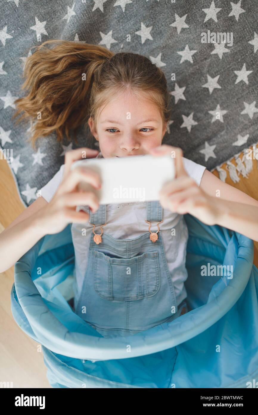 Ritratto di sorridente ragazza sdraiata in un tunnel di tessuto blu sul pavimento a casa prendendo selfie con il telefono cellulare Foto Stock