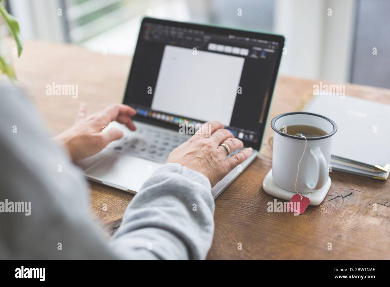 Donna che lavora su un computer portatile, con una tazza di tè sul lato Foto Stock