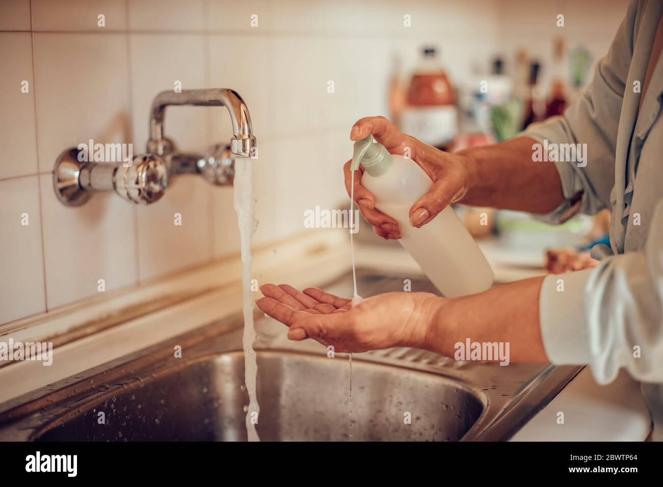 Primo piano di una donna che le lava le mani con sapone e acqua nel lavabo della cucina Foto Stock