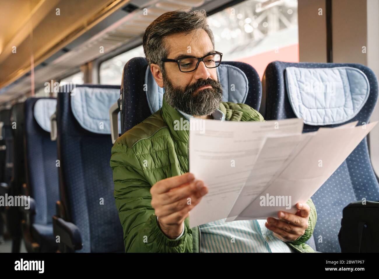 Uomo seduto in treno che legge documenti Foto Stock