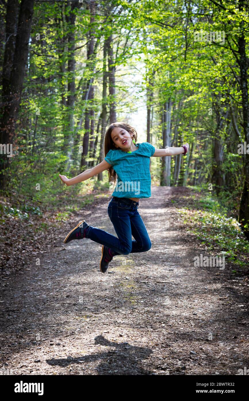 Ritratto di ragazza che salta in aria sulla pista forestale Foto Stock