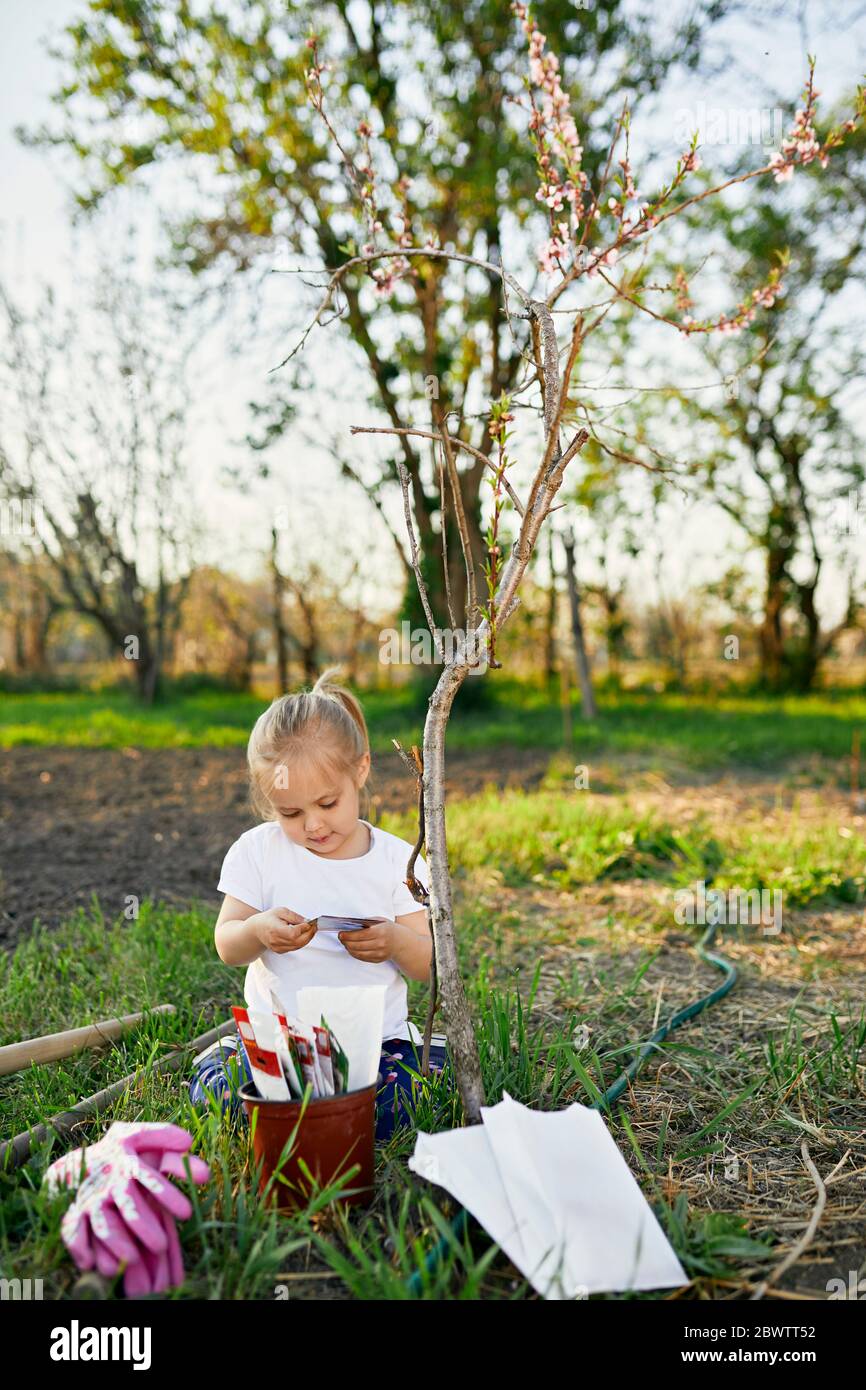 Ragazza cute che legge mentre inginocchiato da pianta a giardino Foto Stock