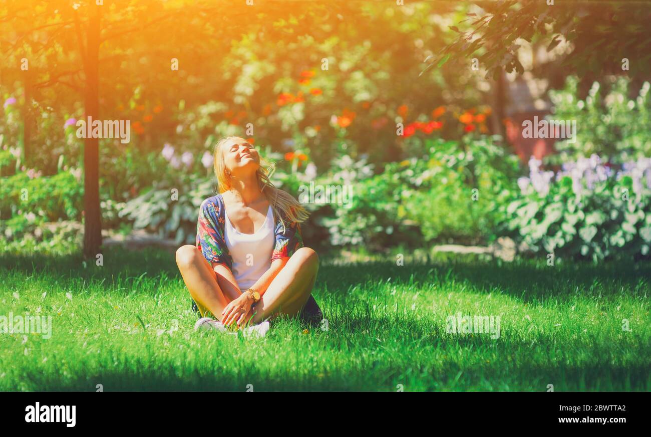 Felice libera giovane donna seduta all'aperto in posizione yoga con gli occhi chiusi sul parco estivo erba calma ragazza godere sorriso e rilassarsi in primavera aria della città. Min Foto Stock