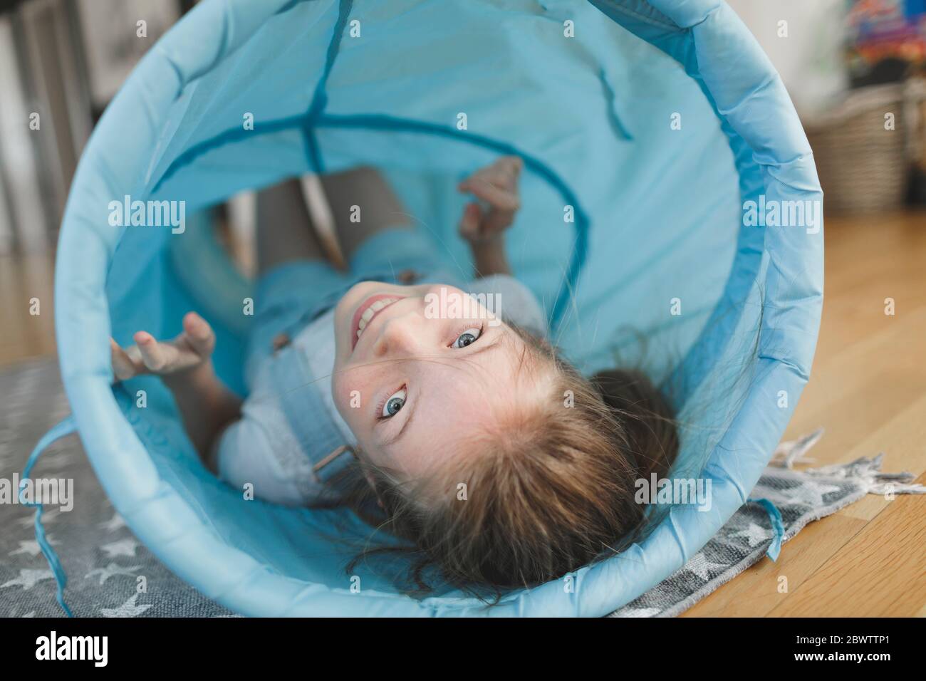 Ragazza sorridente che gioca con il tunnel di tessuto blu a casa Foto Stock