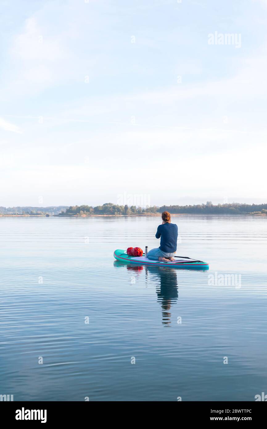 Donna seduta su tavola sup al mattino su un lago Foto Stock
