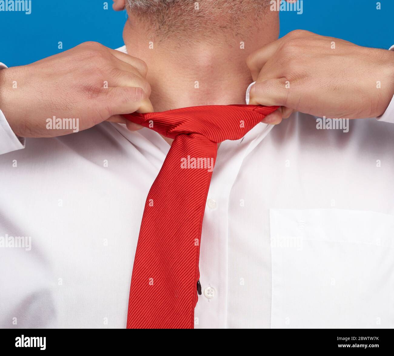 l'uomo in una camicia bianca da ufficio strappa un filo rosso satinato dal collo su sfondo blu, concetto di depressione, disoccupazione e licenziamento Foto Stock