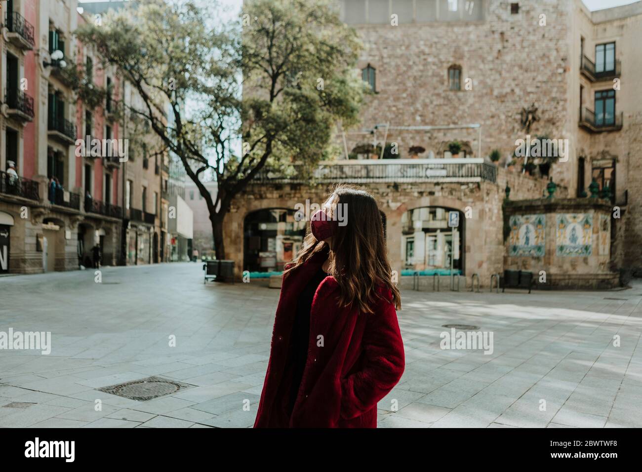 Donna che indossa una maschera che guarda lontano mentre si sta in piedi contro la costruzione del quartiere Gotico durante l'isolamento, Barcellona, Spagna Foto Stock