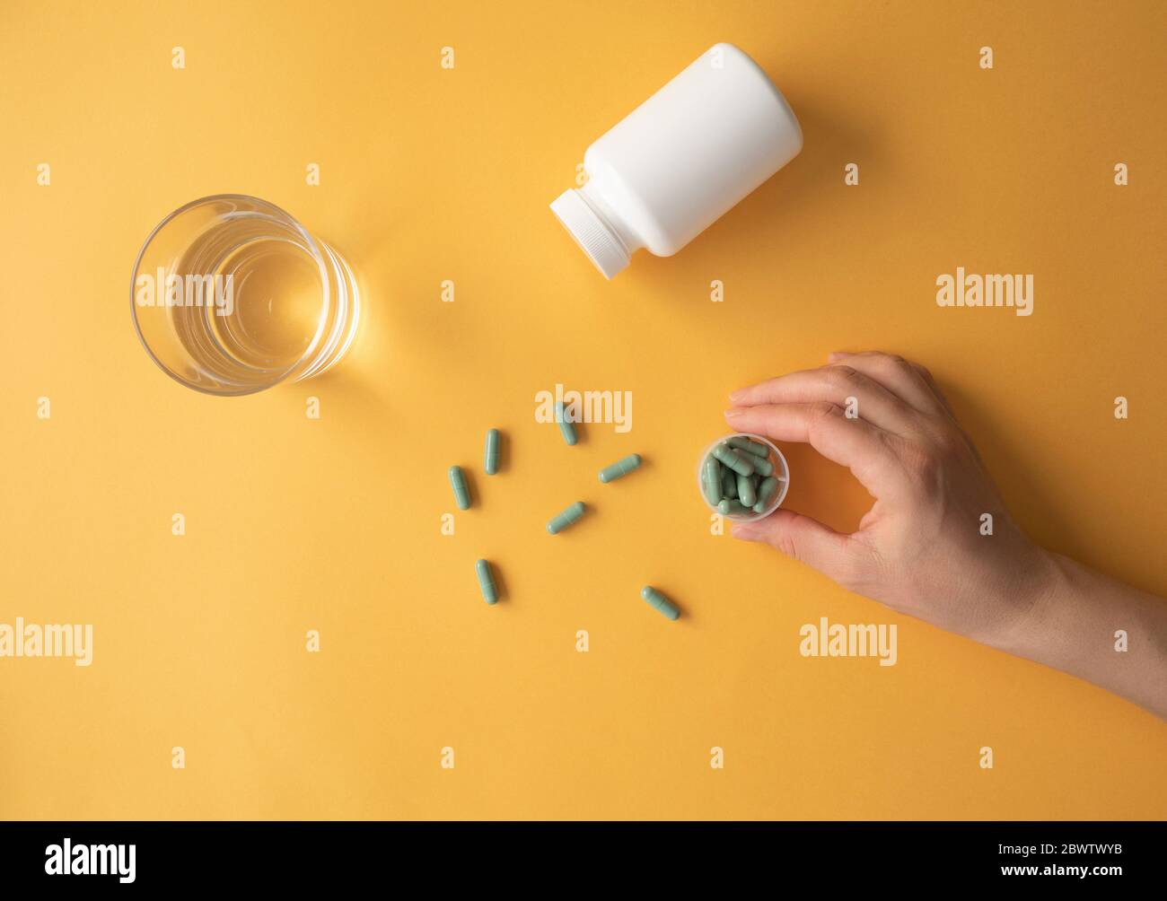 Studio shot di un bicchiere d'acqua e mano di donna che prende capsule nutrizionali di supplemento Foto Stock