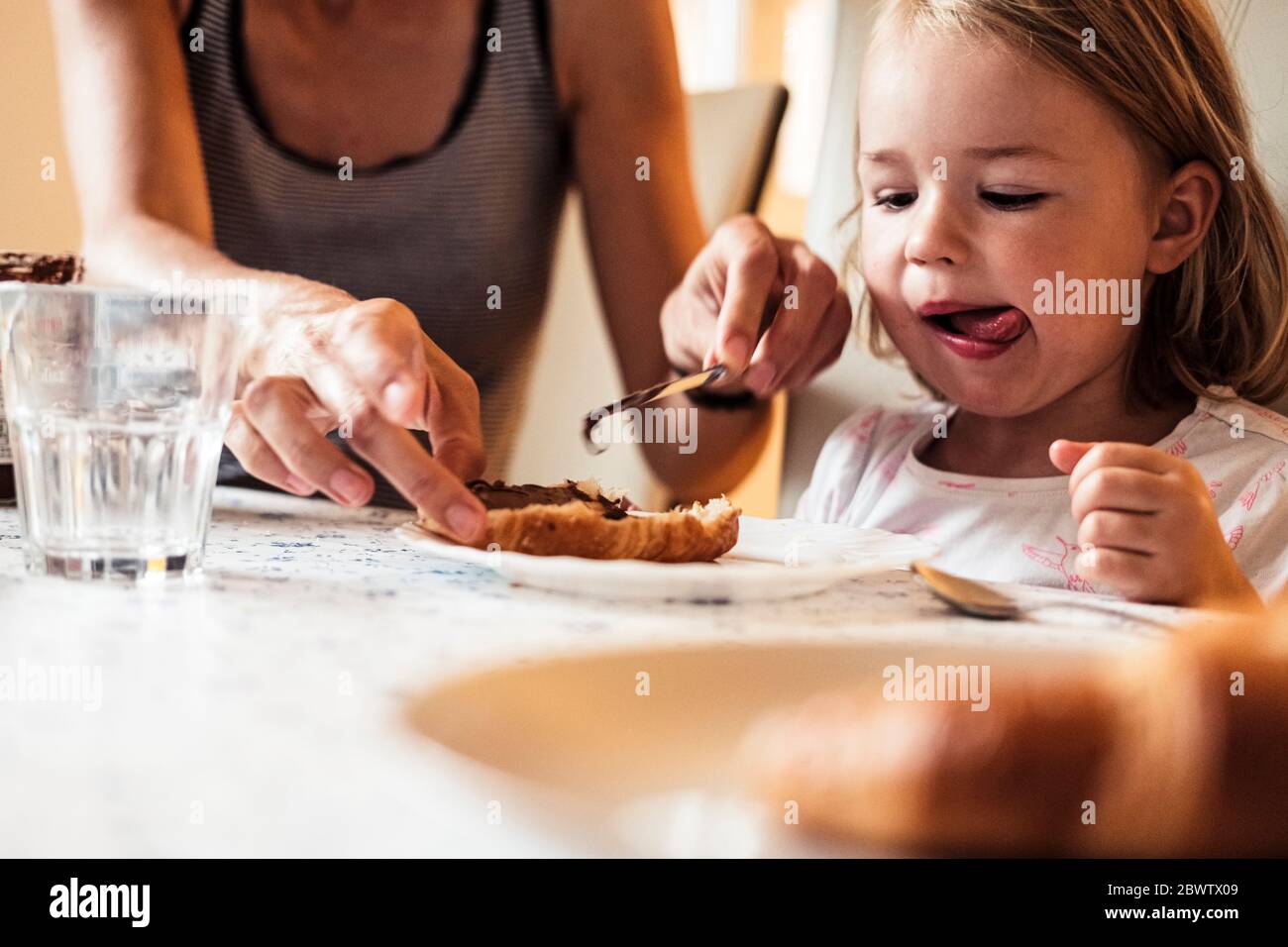 Ritratto di bambina che guarda la madre che diffonde crema di cioccolato sul croissant Foto Stock