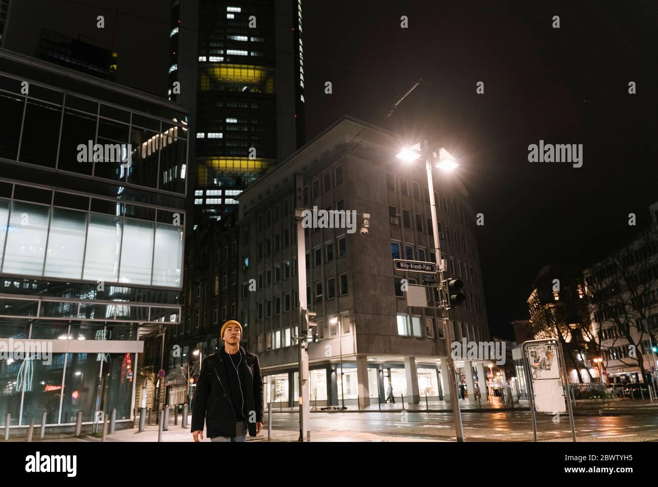 Uomo con cappello giallo e auricolari che cammina in città di notte Foto Stock