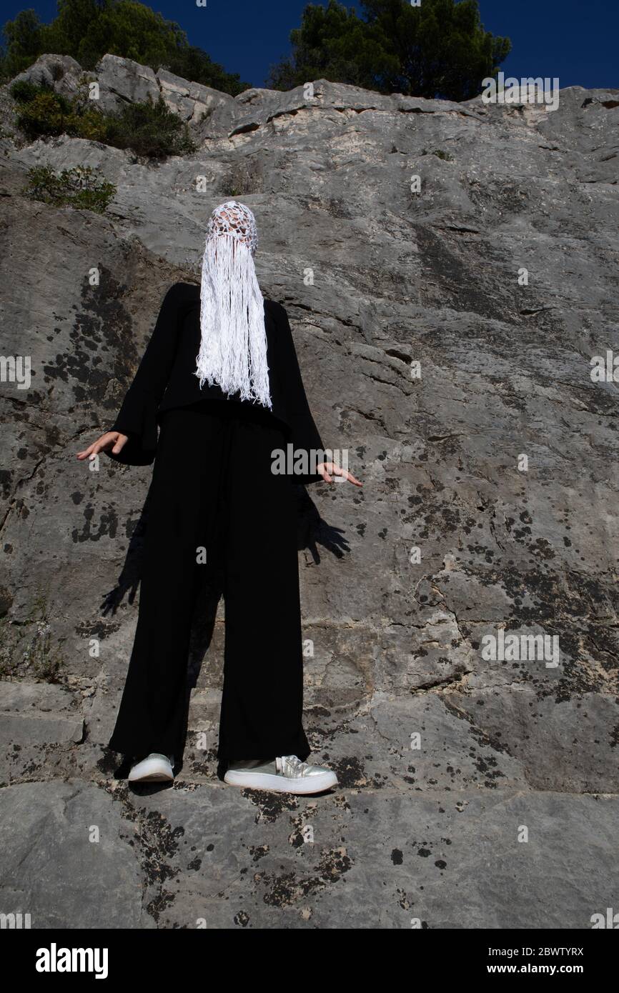 Donna vestita di nero con copricapo bianco e frange in piedi davanti alla parete rocciosa Foto Stock