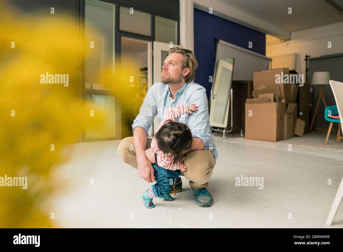 Padre distratto con figlia accovacciata sul pavimento Foto Stock
