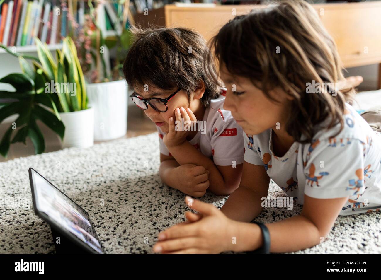 Due fratelli che si trovano sul pavimento a casa utilizzando un tablet digitale per le chat video con la madre Foto Stock