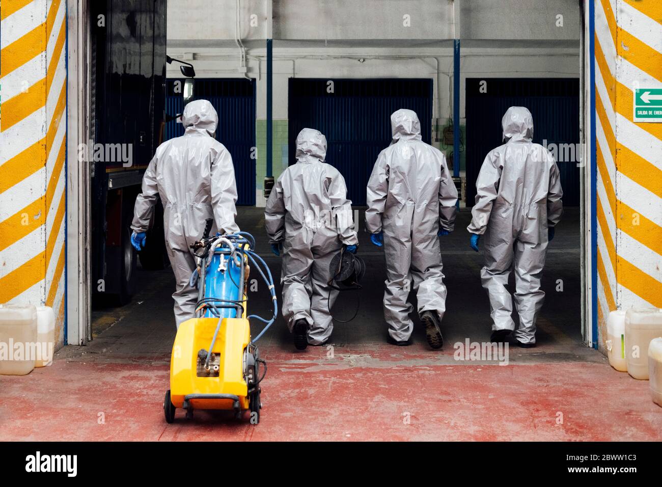 Vista posteriore dei colleghi addetti alla sanificazione che entrano in magazzino con il prodotto chimico decontaminato Foto Stock