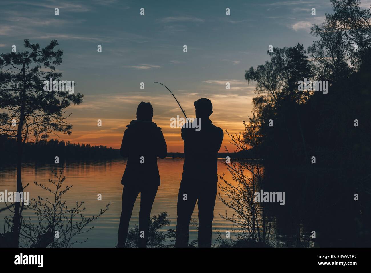 Coppia in piedi al lago, pesca in lago al tramonto Foto Stock
