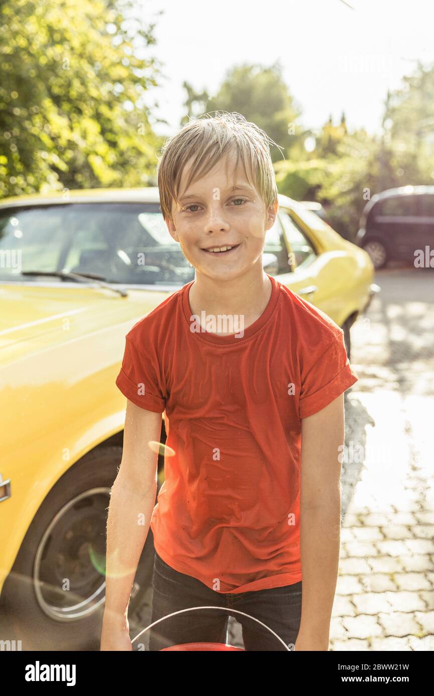 Ritratto di ragazzo bagnato dopo l'acqua lotta in piedi davanti a auto gialla vintage Foto Stock