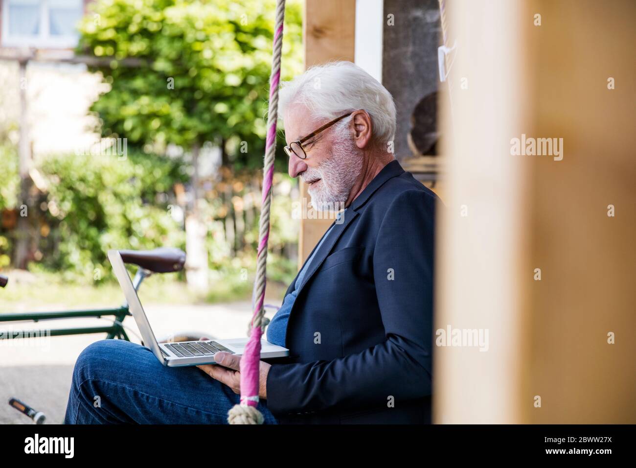 Uomo anziano seduto all'aperto guardando il computer portatile Foto Stock