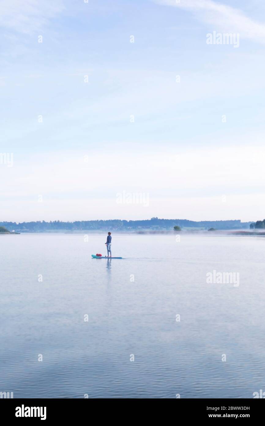 Donna in piedi su sup bordo al mattino su un lago Foto Stock