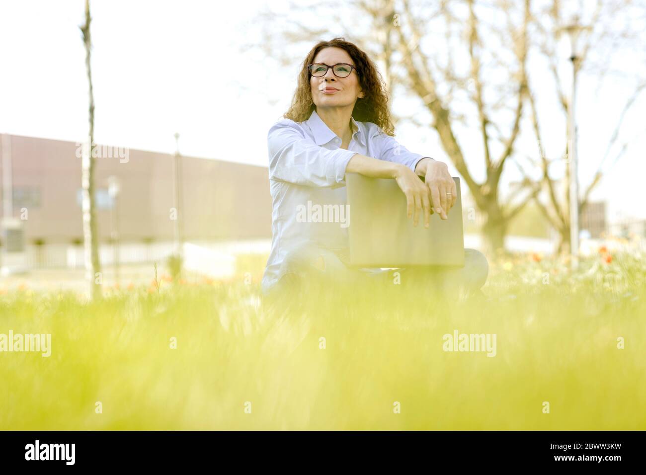 Ritratto di donna con un computer portatile seduto su un prato che guarda a distanza Foto Stock