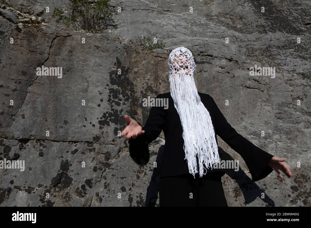 Donna che indossa un copricapo bianco con frange davanti alla parete rocciosa Foto Stock