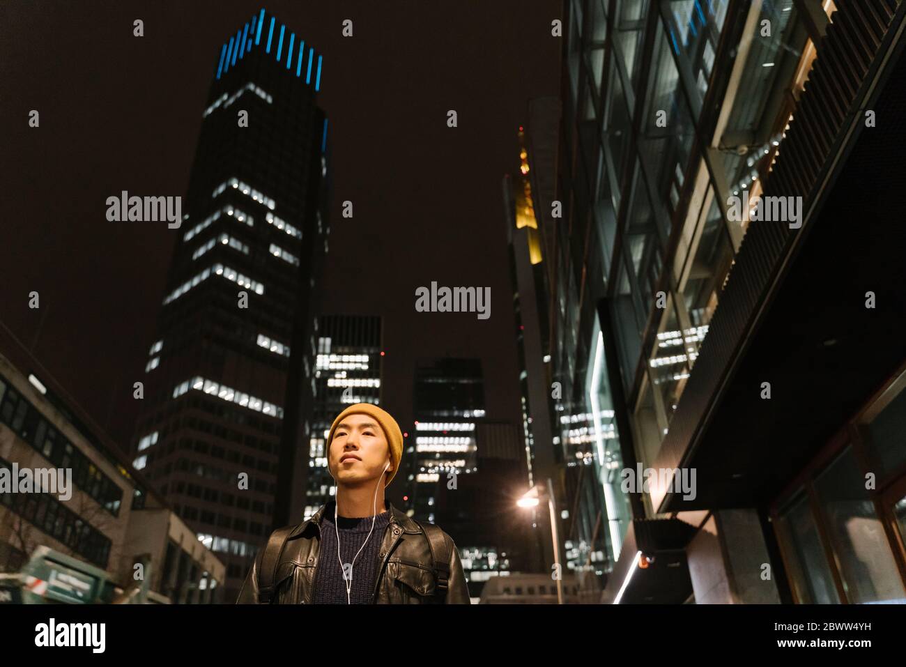 Ritratto di un uomo elegante con cappello giallo e auricolari in città di notte Foto Stock