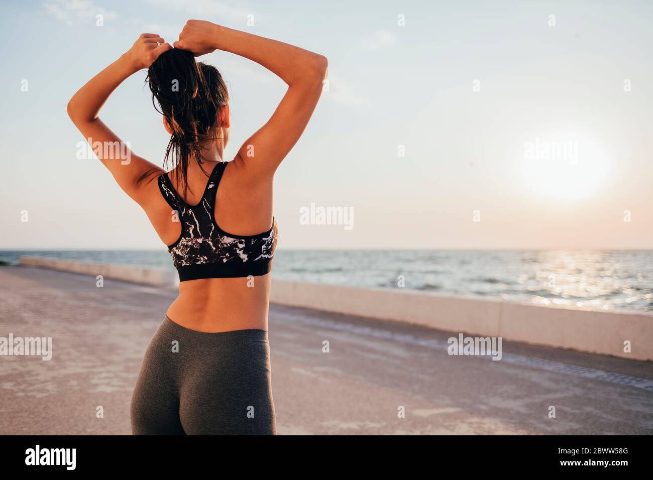 Vista posteriore della giovane atleta che allina i capelli mentre si sta in piedi sulla passeggiata Foto Stock