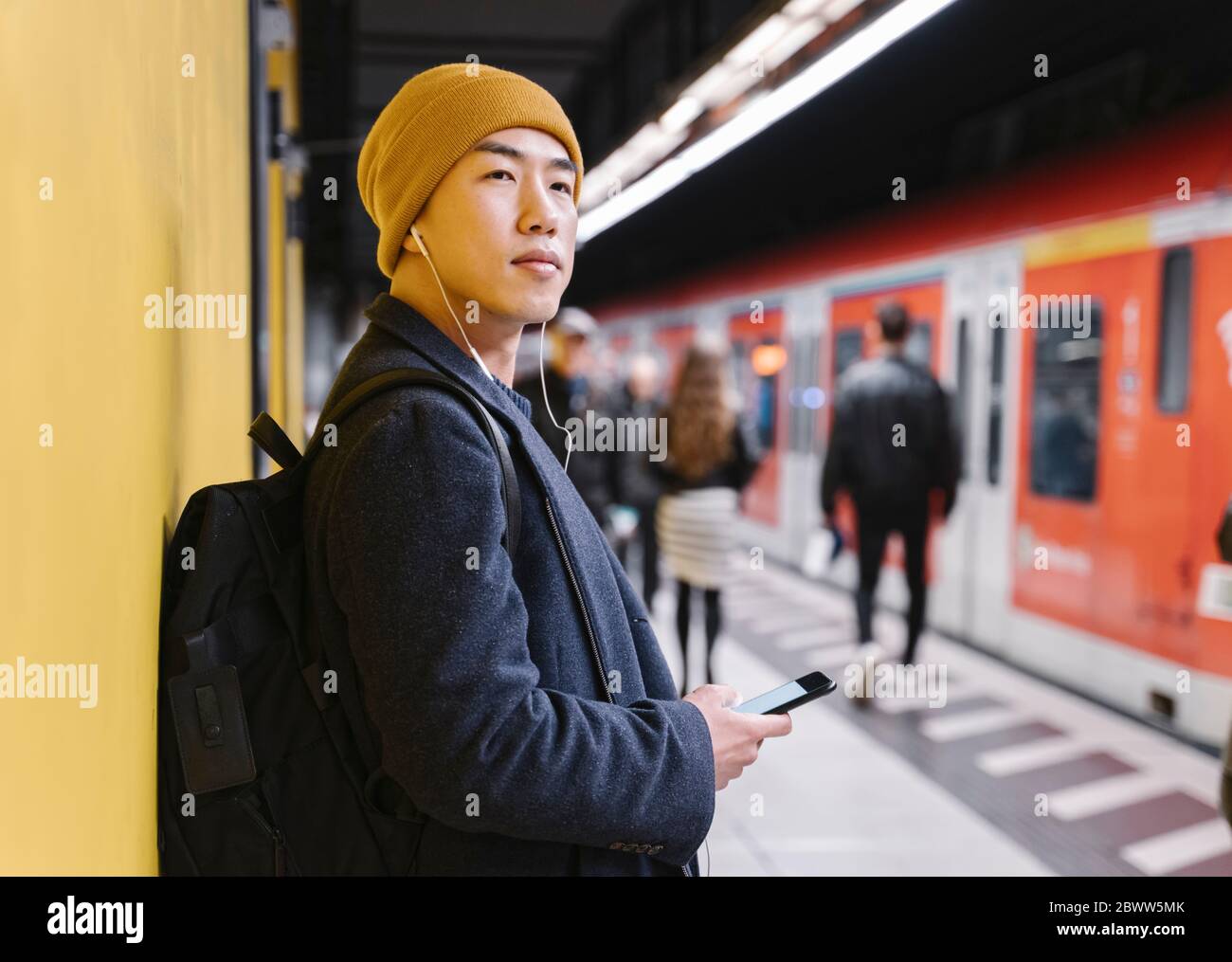 Uomo elegante con cappello giallo e auricolari nella stazione della metropolitana Foto Stock