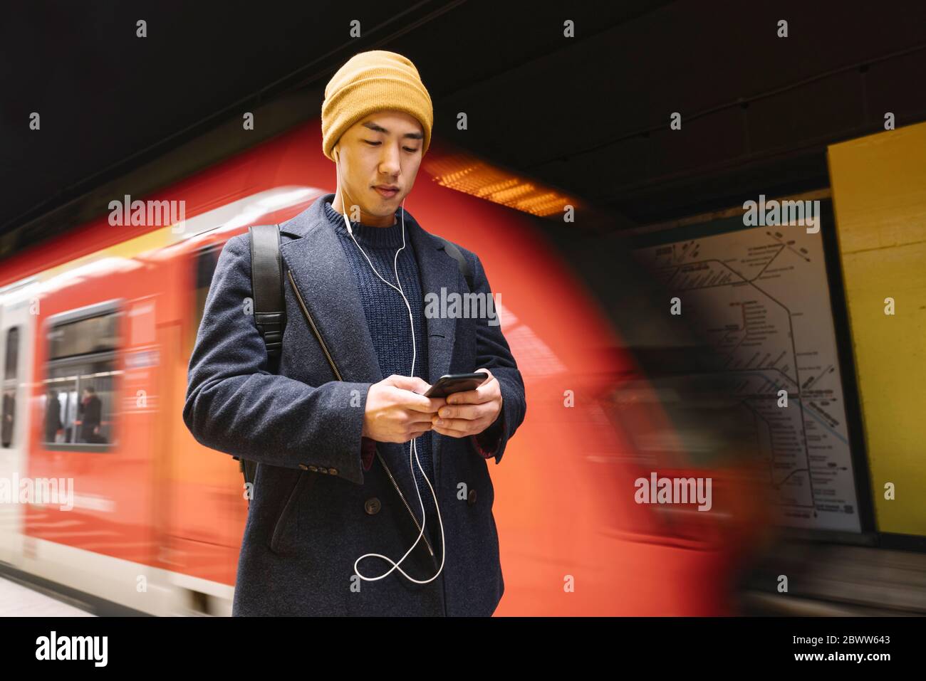 Uomo elegante con smartphone e auricolari nella stazione della metropolitana Foto Stock