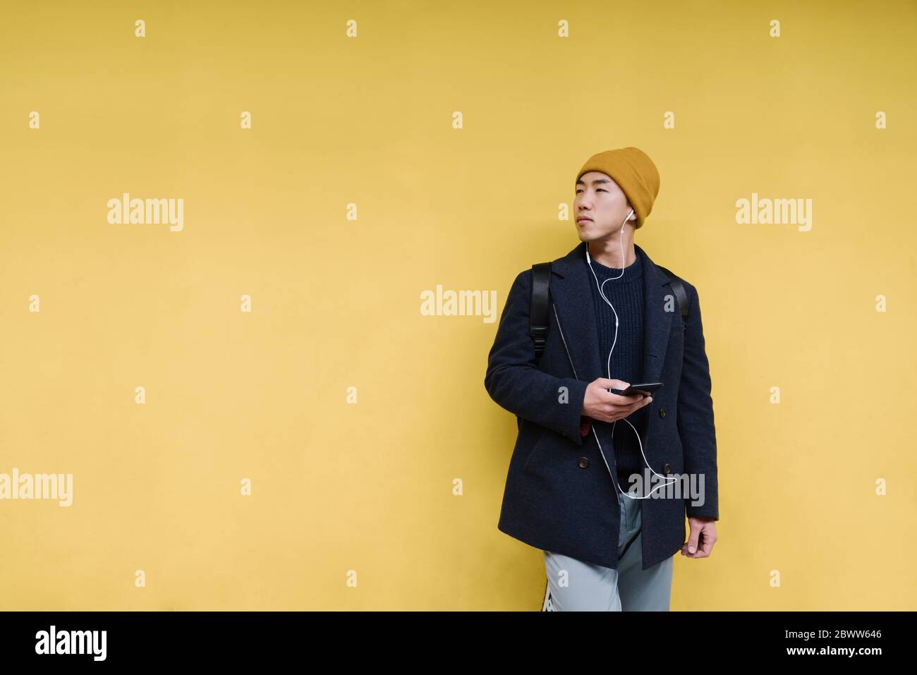 Uomo elegante con cappello giallo e auricolari che utilizzano lo smartphone Foto Stock